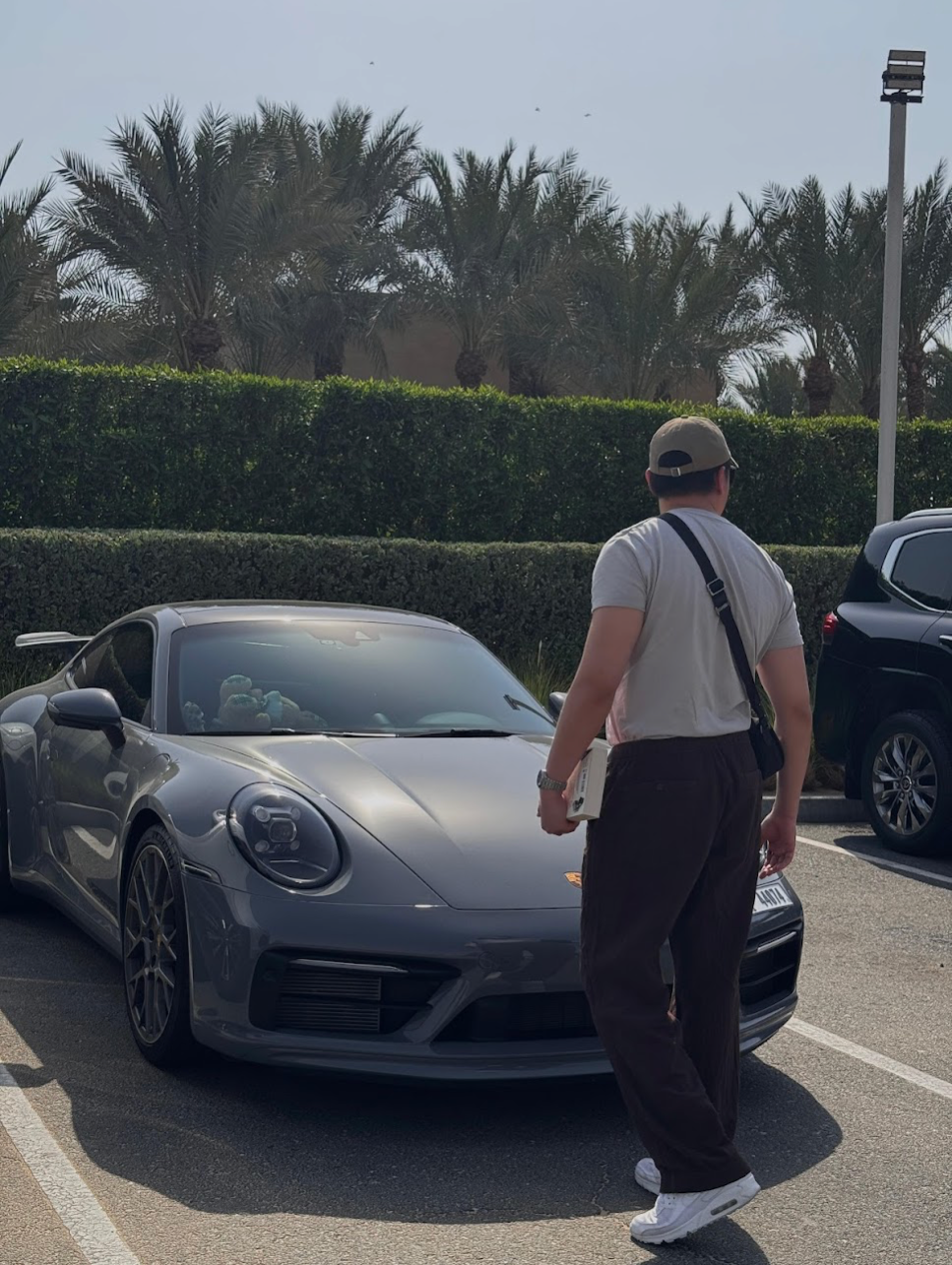 Leonard walking next to a grey Porsche 911